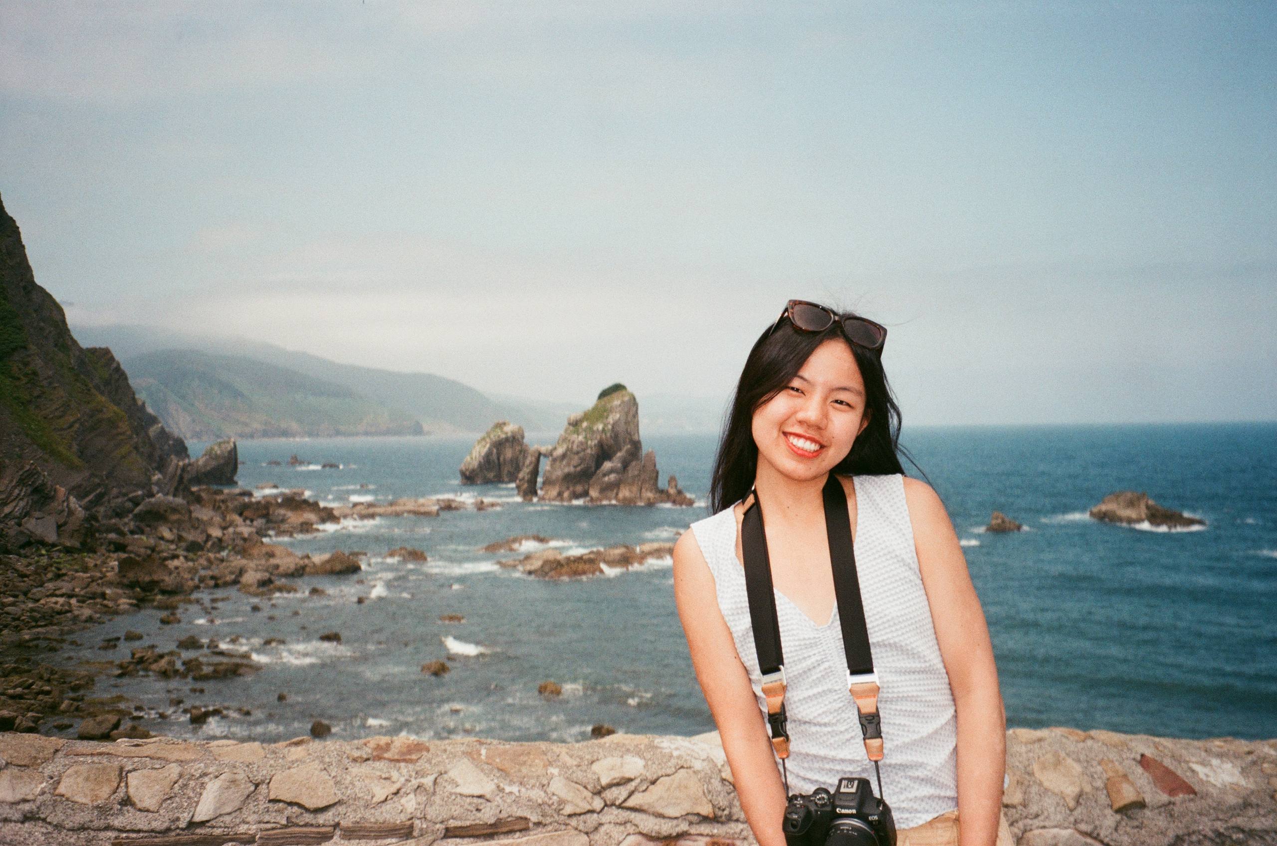 Xinyi smiling by a rocky coastline